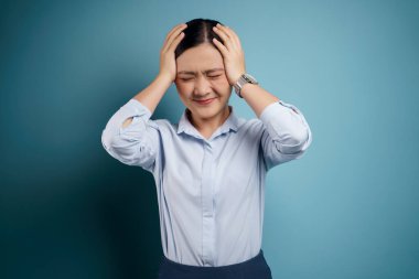 Asyalı kadın hastaydı, baş ağrısı vardı. Kafasına dokunuyordu. Mavi arka plandaydı..