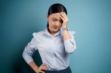 Asyalı kadın hastaydı, baş ağrısı vardı. Kafasına dokunuyordu. Mavi arka plandaydı..