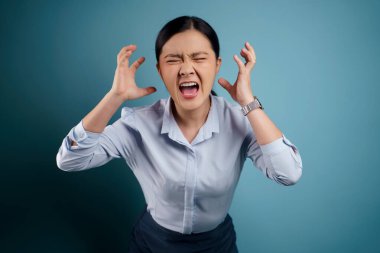 Asyalı kadın öfkeli ve bağırıyor mavi arka planda..