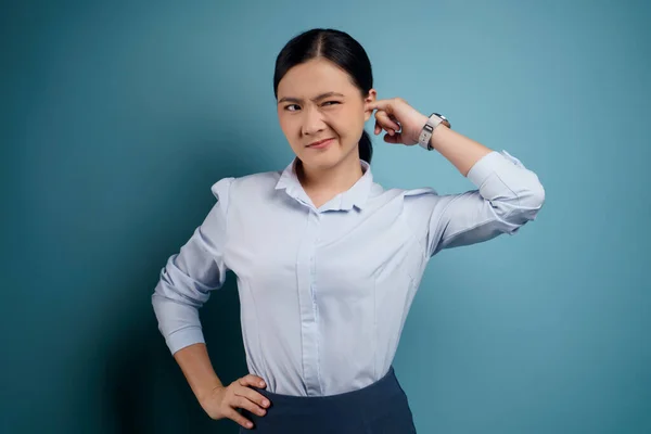 Asian woman itching and putting a finger into her ears standing isolated over blue background.