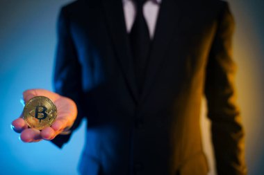 Siyah takım elbiseli bir iş adamının arka planda izole edilmiş altın para tutarken yakın plan çekimi..