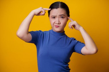 Kafası karışmış Asyalı kadın sarı arka planda tek başına düşünüyor ve ayakta duruyor..