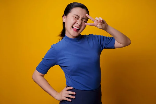 アジアの女性は黄色の背景に隔離された2本の指で平和サインを示す陽気な幸せ — ストック写真
