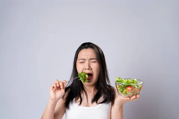 Asian woman trying to eat salad for diet isolated over white background. Healthy lifestyle with Clean food concept.