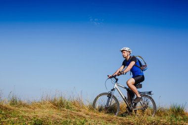 Genç adam yeşil çayır kırsal bir yolda Bisiklete binme