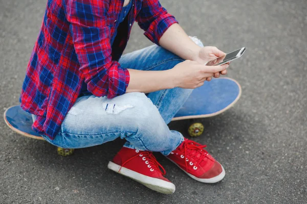 Unga hipster flicka sitter på skatepark och chattar på sin telefon — Stockfoto