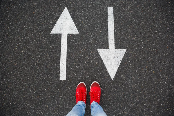 Red sneakers on the asphalt road with drawn arrows pointing to two directions. Making decisions and making choices