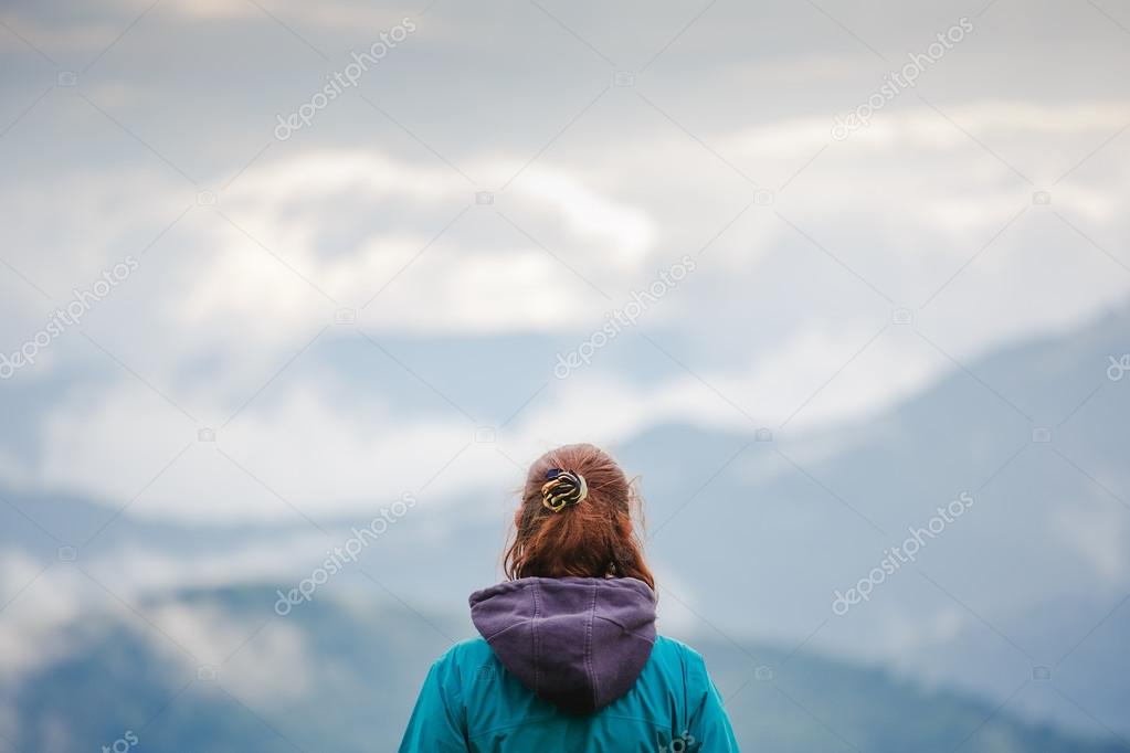 Hiker woman enjoying landscape of cloudy mountains, rear view