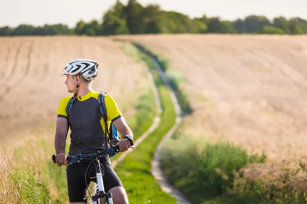 Jovem pedalando em uma estrada rural através do pôr do sol verão prado — Fotografia de Stock