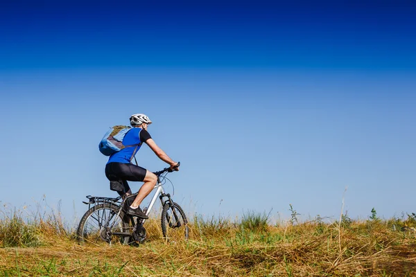Joven ciclismo en un camino rural a través del prado verde — Foto de Stock
