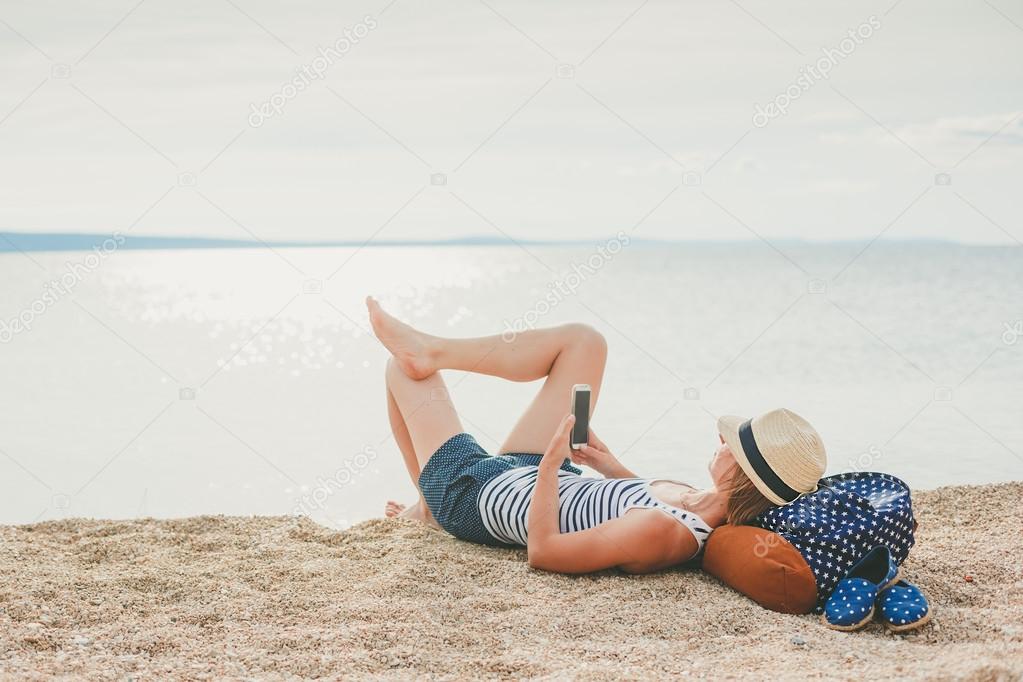 Young hipster girl texting in a smartphone on the beach with the sea in the background