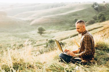 Dağın tepesinde dizüstü bilgisayarla çalışmaktan zevk alan bir adam. Uzak çalışma ya da serbest yaşam tarzı kavramı.