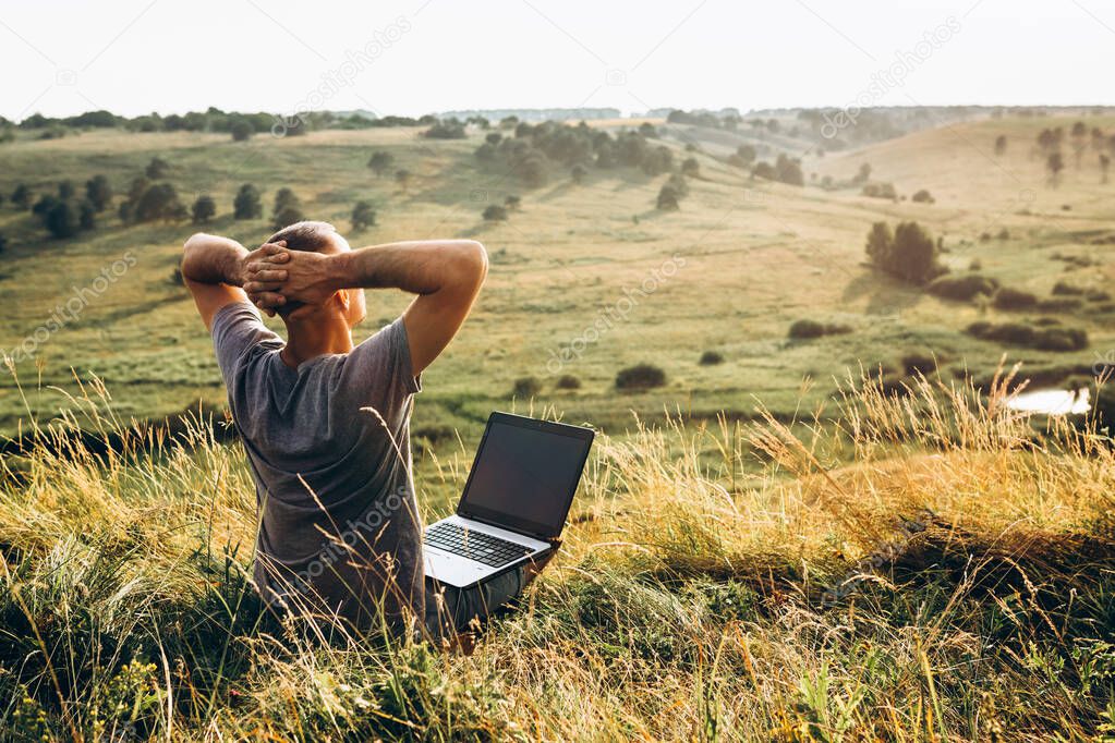 Man enjoying working outdoors with laptop sitting in mountains. Concept of remote work or freelancer lifestyle.
