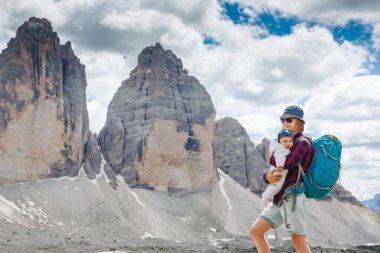 Sırt çantasıyla seyahat eden küçük bir çocukla genç bir anne. Anne çocukla gezintiye çıktı, aile gezisi dağlarda. Ulusal Park Tre Cime di Lavaredo, Dolomite Dağları, İtalya
