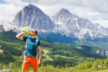 Yürüyüşçü Adam arka planda Dolomitlerle yürüdükten sonra dinleniyor ve su içiyor, İtalya.