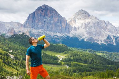 Arka planda Dolomites dağlarıyla yürüdükten sonra dinlenen ve su içen adam, İtalya.