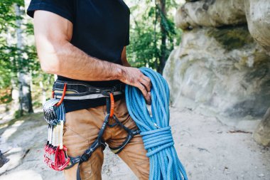 Güçlü bir dağcının yakın çekimi kemerinde ekipmanla halat tutarak tırmanmaya hazırlanıyor.