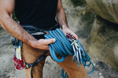 Güçlü bir dağcının yakın çekimi kemerinde ekipmanla halat tutarak tırmanmaya hazırlanıyor.