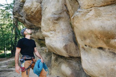 Güçlü bir tırmanıcı kemerinde ekipmanla halat tutuyor ve tırmanmaya hazırlanıyor.