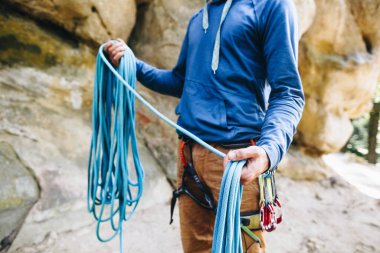 Güçlü bir dağcının yakın çekimi kemerinde ekipmanla halat tutarak tırmanmaya hazırlanıyor.