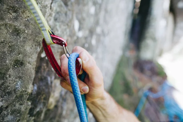Close up of rock climber hand clipping rope in a quick draw caribener on a cliff face