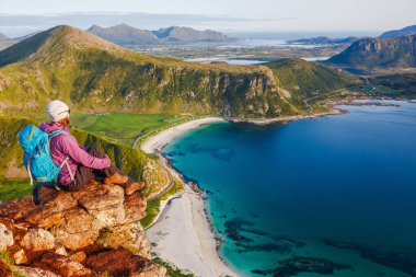 Woman hiker relaxing at the top of the mountain and looking at incredible views of a Norwegian fjord, Lofotens. Travel, adventure, healthy lifestyle concept clipart