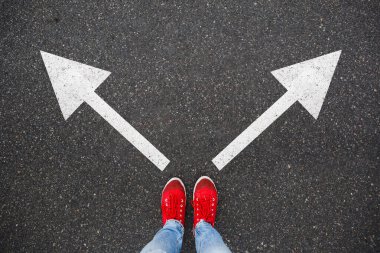 Asfalt yolda kırmızı spor ayakkabılar ve iki yöne doğru çizilmiş oklar. Karar vermek ve seçim yapmak, ikilem kavramı