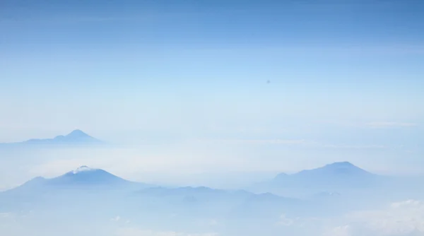 Luchtfoto van blauwe hemel met wolken en mist rond de bergen — Stockfoto