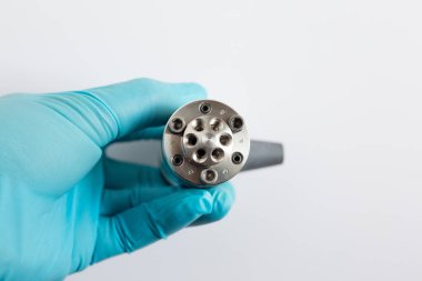 Mavi eldivenli bir bilim adamının elinde 6-port HPLC enjektörü var. Sıvı kromatografi montajı veya beyaz arkaplanda bakım için bağlantı portlarını gösteren yakın plan.