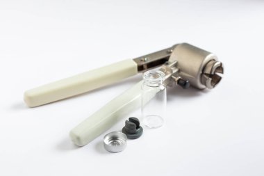 Lastik septum ve alüminyum kapaklı cam bir otomatik ampül, laboratuvar örneklerini mühürlemeye hazır elle kıstırma aracının yanında düzenlenir..