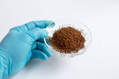 Mavi eldiven giyen bir bilim adamı, bitkisel, botanik ve besin özleri için kullanılan dondurucu kurutma teknolojisi kullanılarak üretilen kahverengi dondurulmuş bir özü içeren cam bir kap tutuyor..