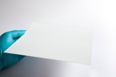 İnce Kromatografi (TLC) plakası boş olan araştırmacının eli yakın plan. Görüntü, kimyasal bileşikleri ayırmak için kullanılan silis jel adsorbent ile kaplı beyaz yüzeye odaklanır..