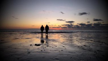 Güzel bir gün batımı kumsalında güneşe doğru yürüyen insan siluetleri.