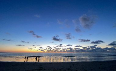 Denizde parlayan batan güneşin görüntüsü sahile yansıyor, güneş gibi parlayan bulutlar. Peyzaj