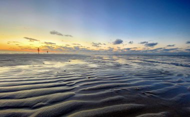 Denizde parlayan batan güneşin görüntüsü sahile yansıyor, güneş gibi parlayan bulutlar. Peyzaj