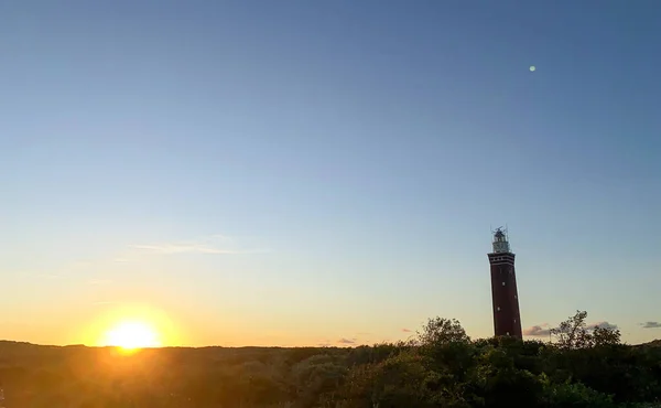 Leuchtturm steht an der holländischen Küste mit einem dramatischen. und farbenfroher Sonnenuntergang oder Sonnenaufgang dahinter — Stockfoto