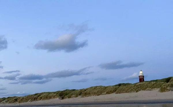 Leuchtturm steht an der holländischen Küste mit einem dramatischen. und farbenfroher Abend- oder Morgenhimmel dahinter — Stockfoto