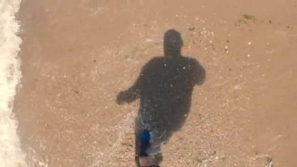 Ombra di un uomo che cammina tra le onde della costa sulla spiaggia — Video Stock