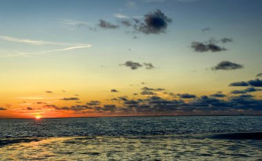 Denizde parlayan batan güneşin görüntüsü sahile yansıyor, güneş gibi parlayan bulutlar. Peyzaj