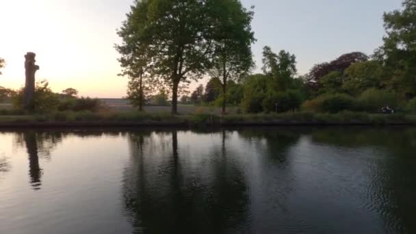 Gün batımında ağaçlarla kaplı güzel nehir kenarı manzarası, güneşi ve dramatik gökyüzünü yansıtıyor. Kontrastlı sahne — Stok video