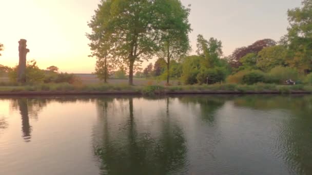 Bela paisagem ribeirinha com árvores ao pôr do sol, refletindo o sol e o céu dramático na água. Cena contrastante — Vídeo de Stock