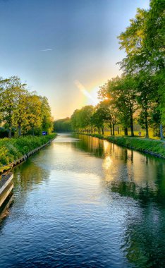 Ağaçlarla çevrili bir su kütlesinin üzerinde dramatik bir gün batımı.