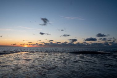 Denizde parlayan batan güneşin görüntüsü sahile yansıyor, güneş gibi parlayan bulutlar. Peyzaj