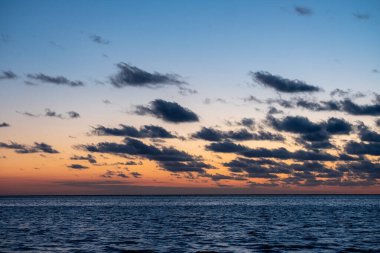 Denizde parlayan batan güneşin görüntüsü sahile yansıyor, güneş gibi parlayan bulutlar. Peyzaj