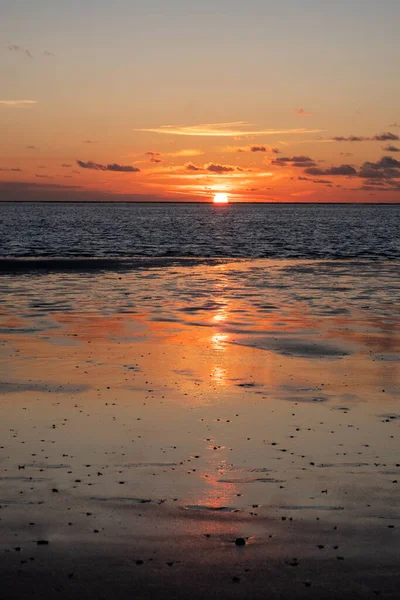 Denizde parlayan batan güneşin görüntüsü sahile yansıyor, güneş gibi parlayan bulutlar. Peyzaj