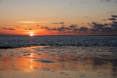 Denizde parlayan batan güneşin görüntüsü sahile yansıyor, güneş gibi parlayan bulutlar. Peyzaj