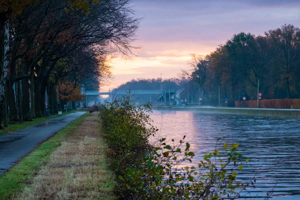 Canal fluvial se tordant avec des berges d'herbe et des fleurs et des arbres sauvages dans un paysage pittoresque lors d'un lever de soleil matinal d'automne brumeux — Photo