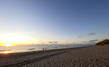 Denizde parlayan batan güneşin görüntüsü sahile yansıyor, güneş gibi parlayan bulutlar. Peyzaj