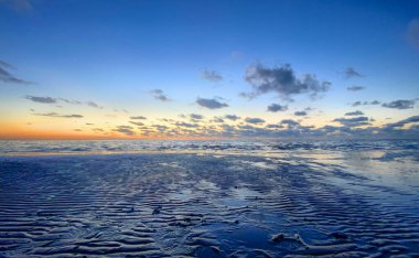 Denizde parlayan batan güneşin görüntüsü sahile yansıyor, güneş gibi parlayan bulutlar. Peyzaj