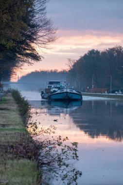 Güneşin doğduğu sisli bir sabahta nehirde kargo gemisi